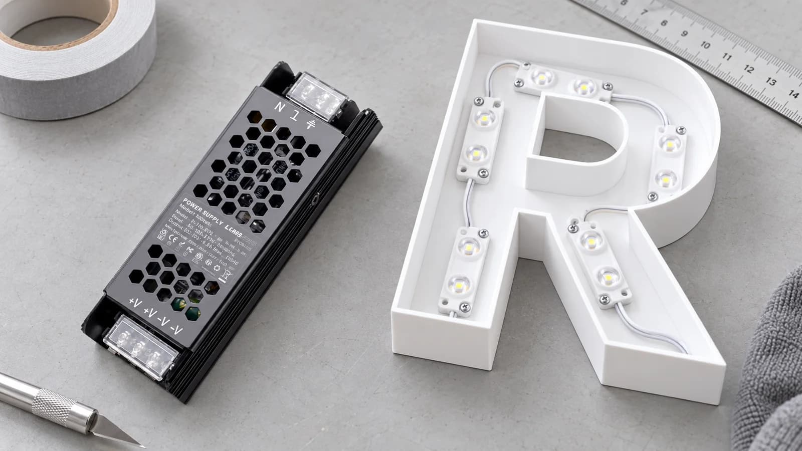 Fuente de poder LED junto a componentes de letras iluminadas en una mesa de trabajo